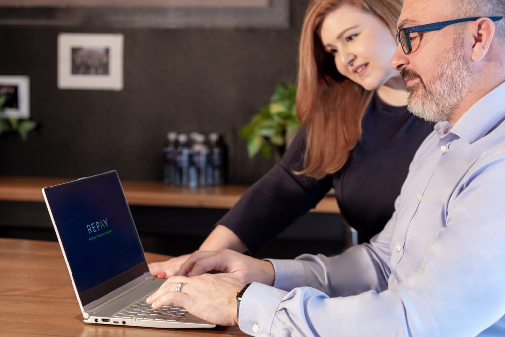 businessman and businesswomen looking at REPAY on laptop