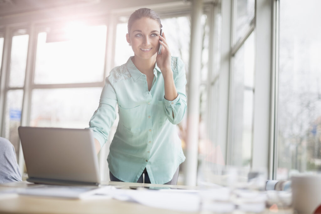 Young businesswoman using laptop and cell phone in office