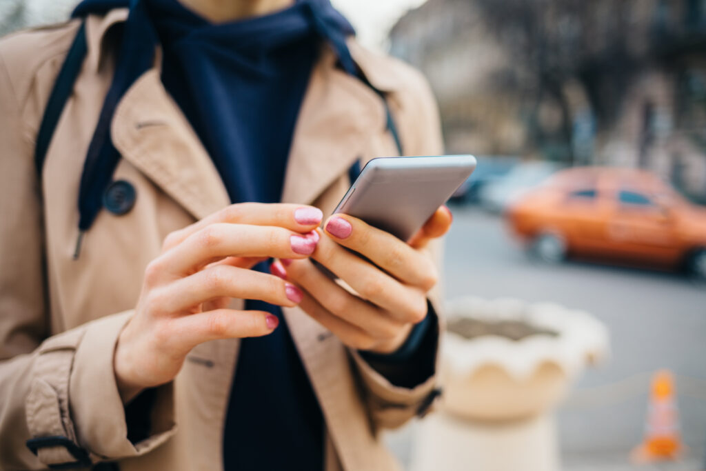 young woman wearing beige coat using smart phone