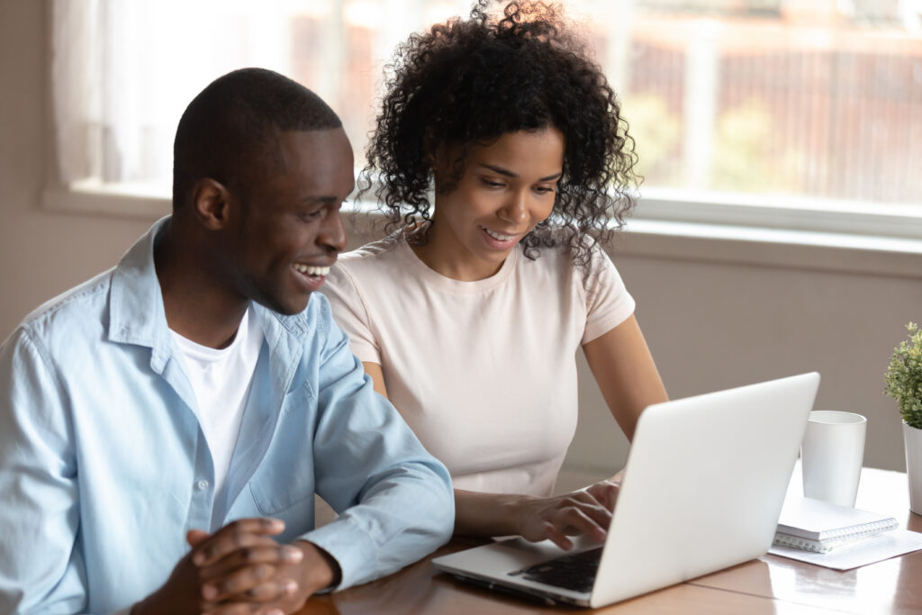 Smiling loving married mixed race couple sitting together looking at laptop computer