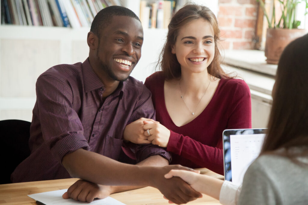 smiling multiracial couple customers shaking hands with mortgage broker